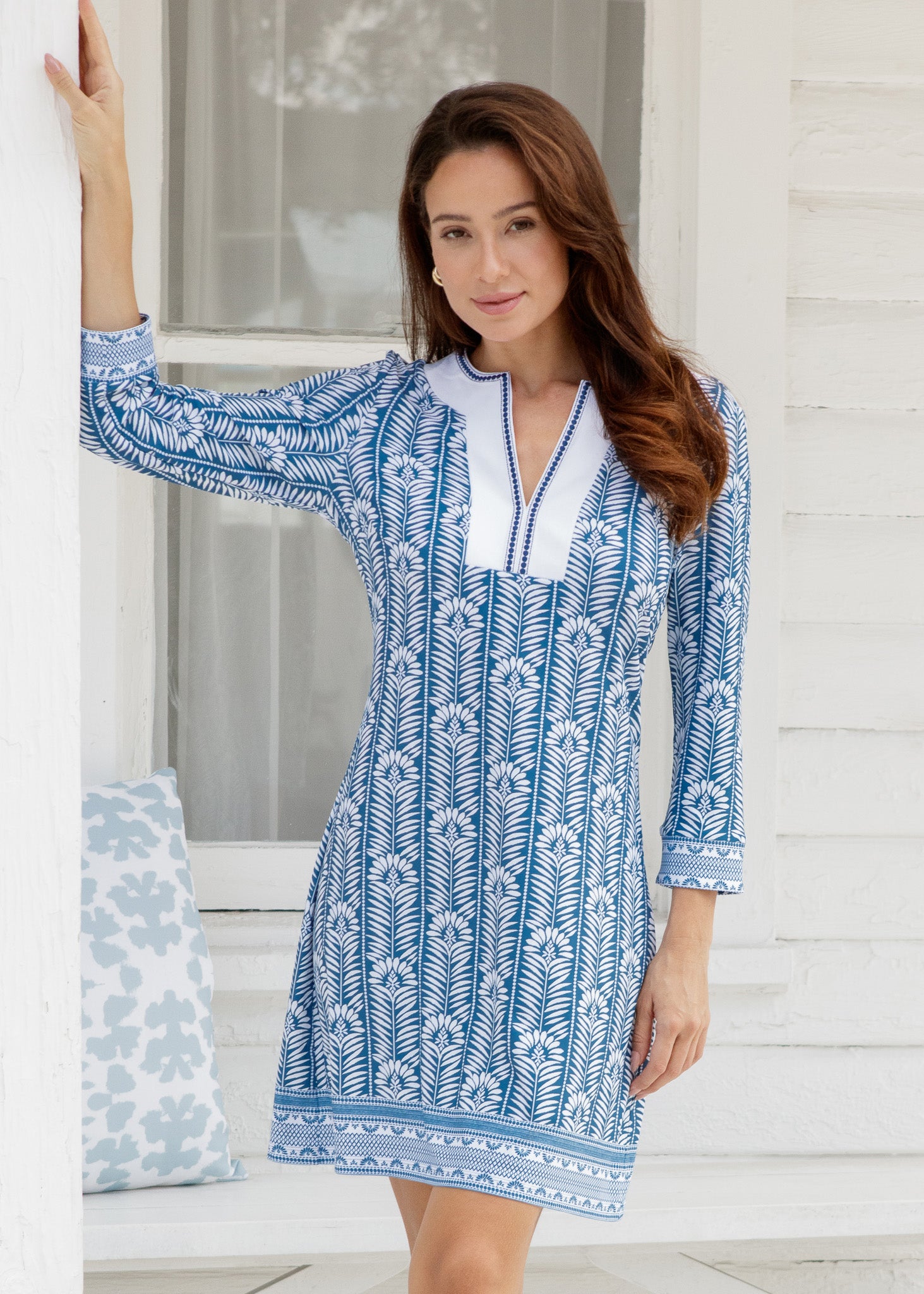 Woman wearing a blue and white patterned dress standing on a porch.