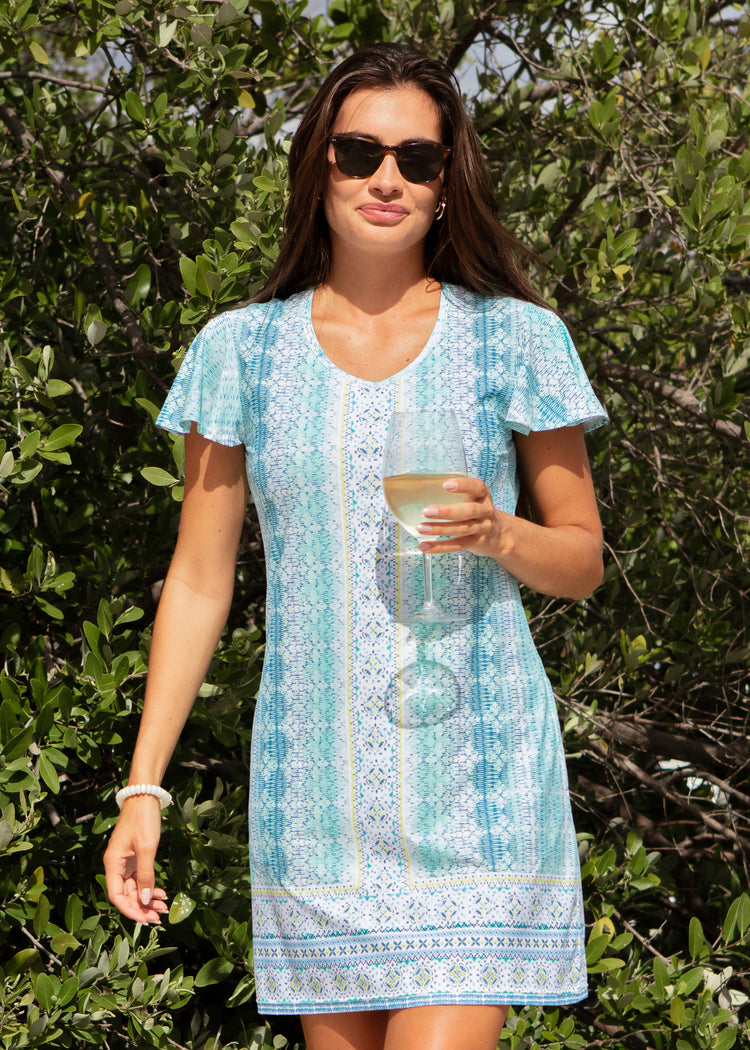 Woman in a light blue dress holding a drink outdoors among greenery