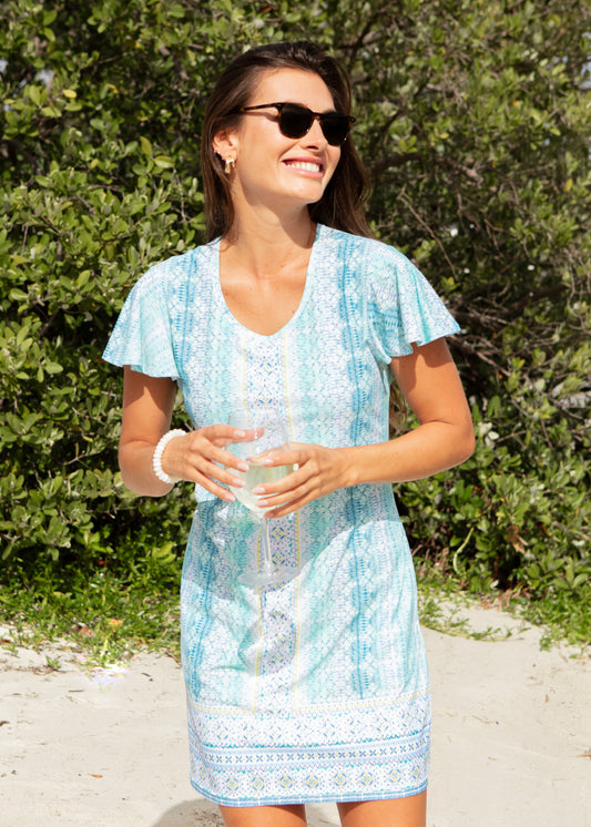 Woman in a light blue dress standing on a beach with greenery in the background