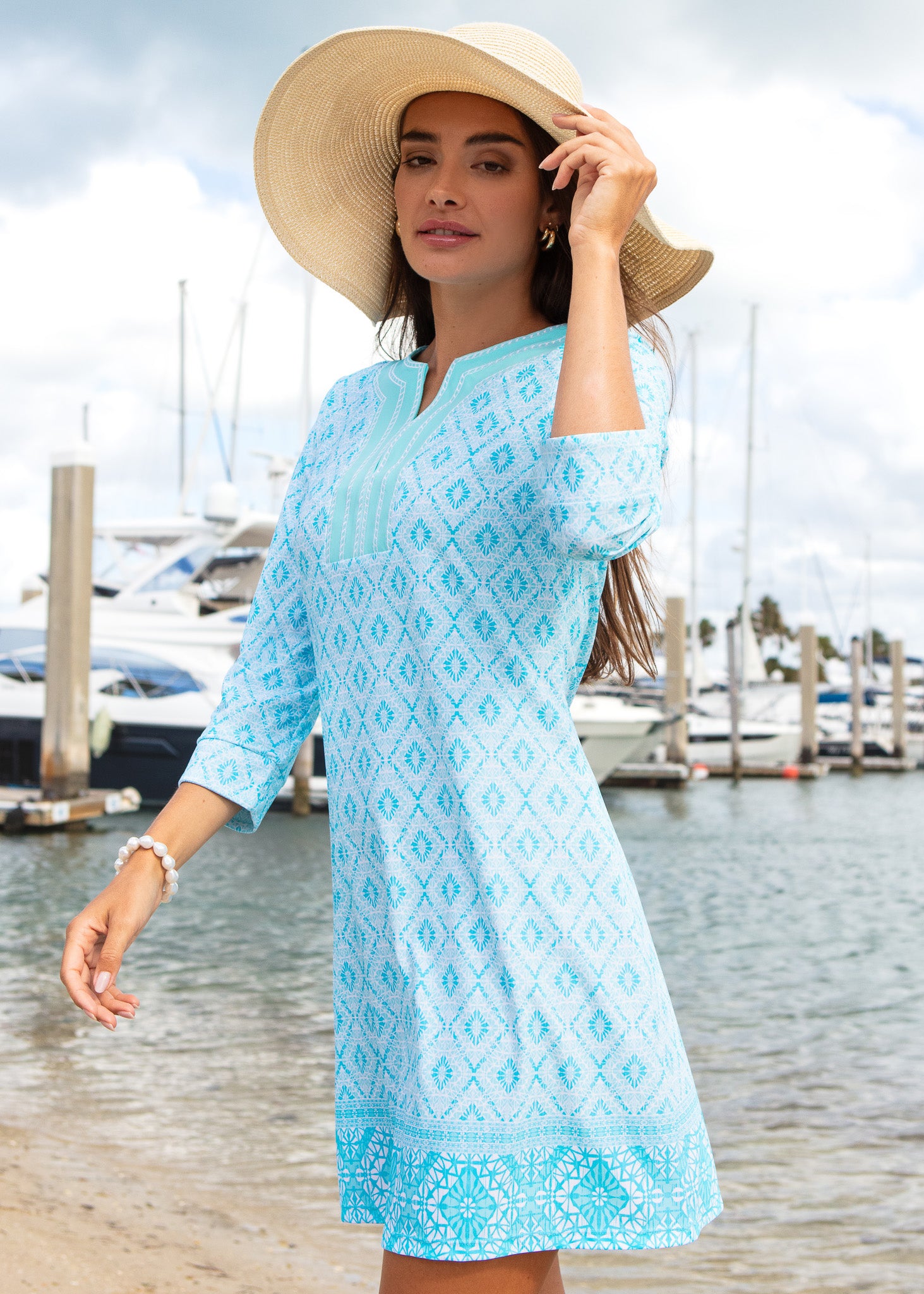 Woman wearing a light blue dress with a pattern, standing by a marina.