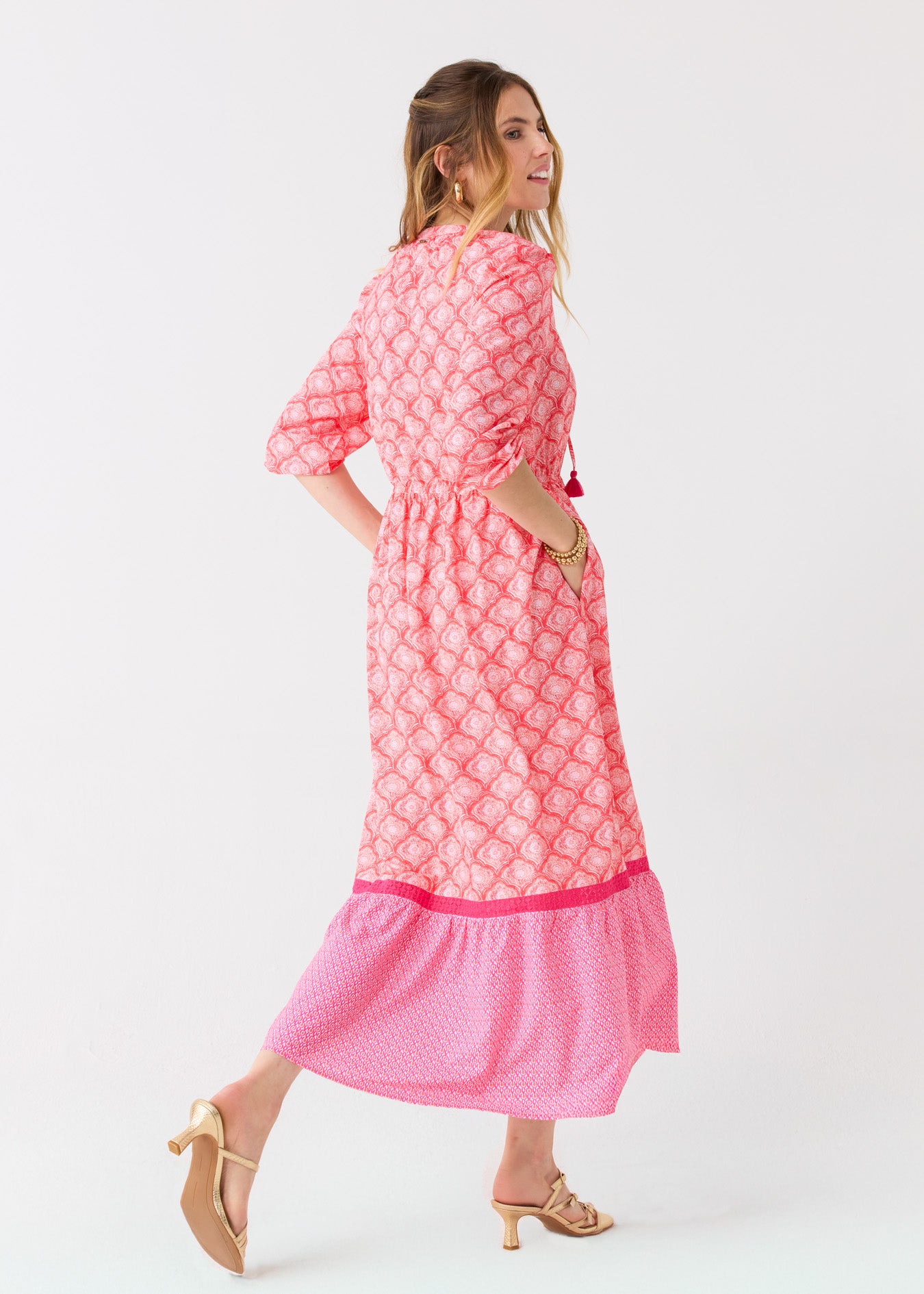 The side of a blonde woman walking with a hand in her pocket in the Cabana Life sun protective Amelia Island Relaxed Maxi Dress with gold sandals.