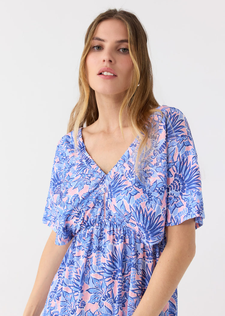 A close up of a blonde woman wearing the Cabana Life sun protective Palm Beach Flutter Sleeve Maxi Dress with a cutout in the middle.