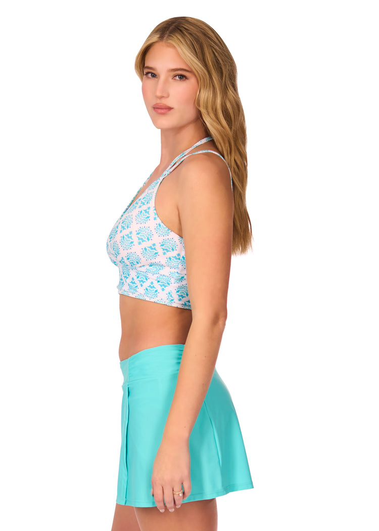 Side of blonde woman wearing Amalfi Coast Reversible Bikini Top with Aqua Classic Swim Skirt on white background.