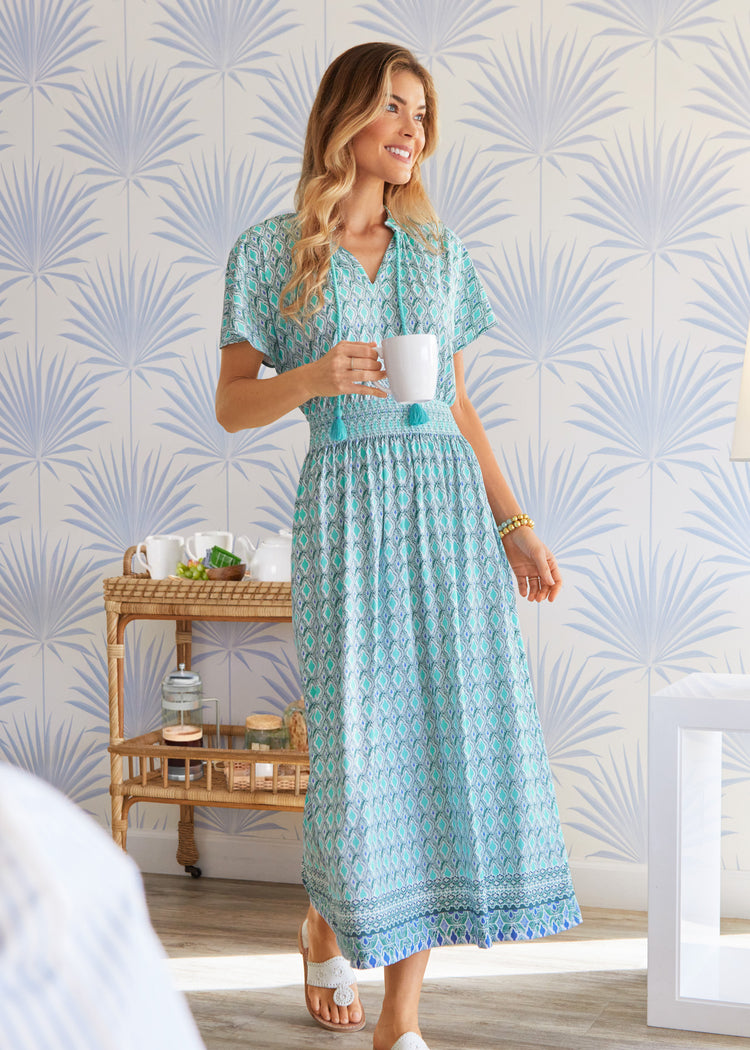 Blonde woman wearing Amalfi Coast Cap Sleeve Maxi Dress inside holding coffee cup.