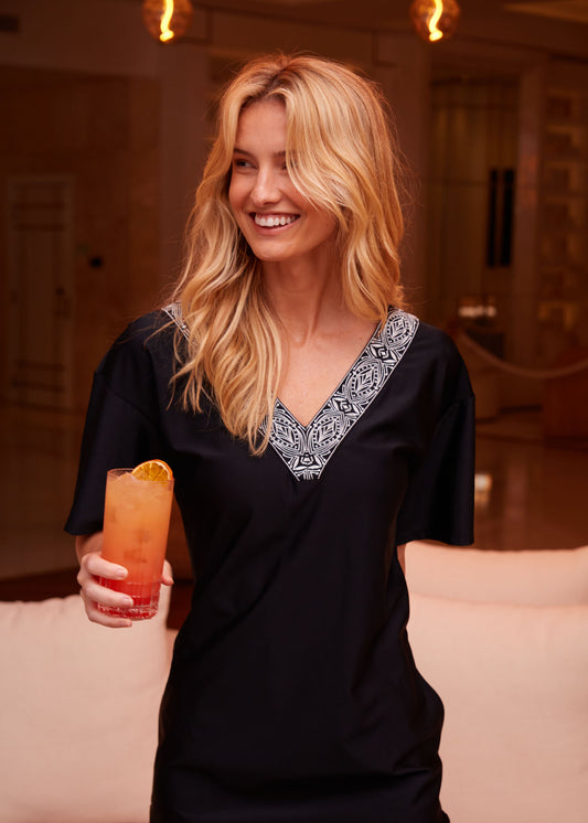 Woman wearing Black Flutter Sleeve Shift Dress holding orange tropical drink.