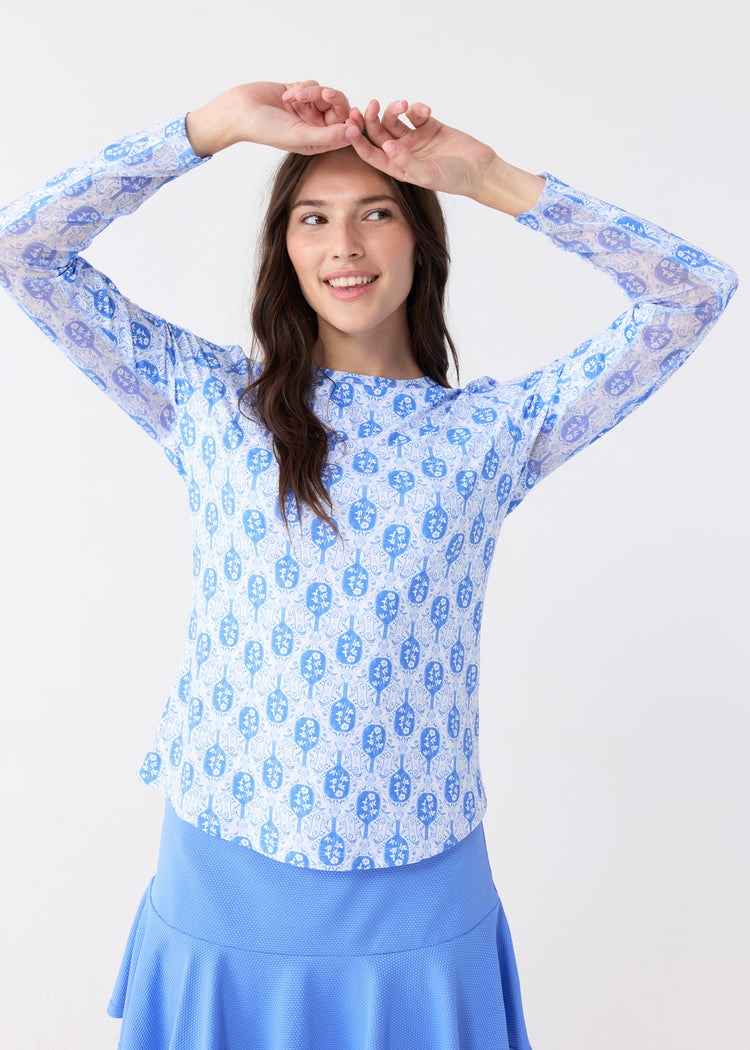 A brunette woman wearing the sun safe Pickleball Long Sleeve Performance Top with printed mesh underarm venting and the Periwinkle 15" Flounce Skort from Cabana Life.