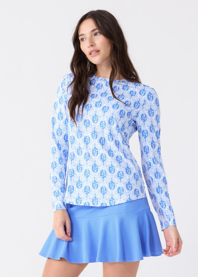 A brunette woman wearing the sun safe Pickleball Long Sleeve Performance Top and Periwinkle 15" Flounce Skort from Cabana Life.