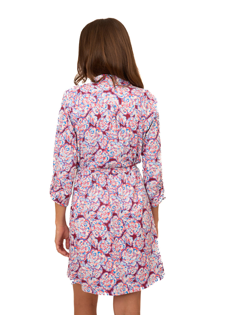 The back of a brunette woman wearing Cabana Life's sun protective Camden Peony Button Down Shirt Dress with sleeves buttoned at a 3/4 length on a white background.