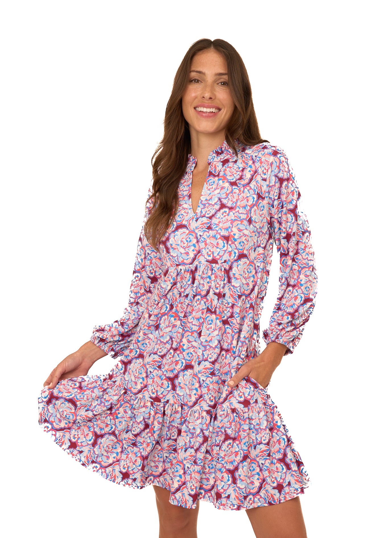 A brunette woman wearing Cabana Life's sun protective Camden Peony Relaxed Dress with her hand in her pocket and the other on the bottom hem on a white background.