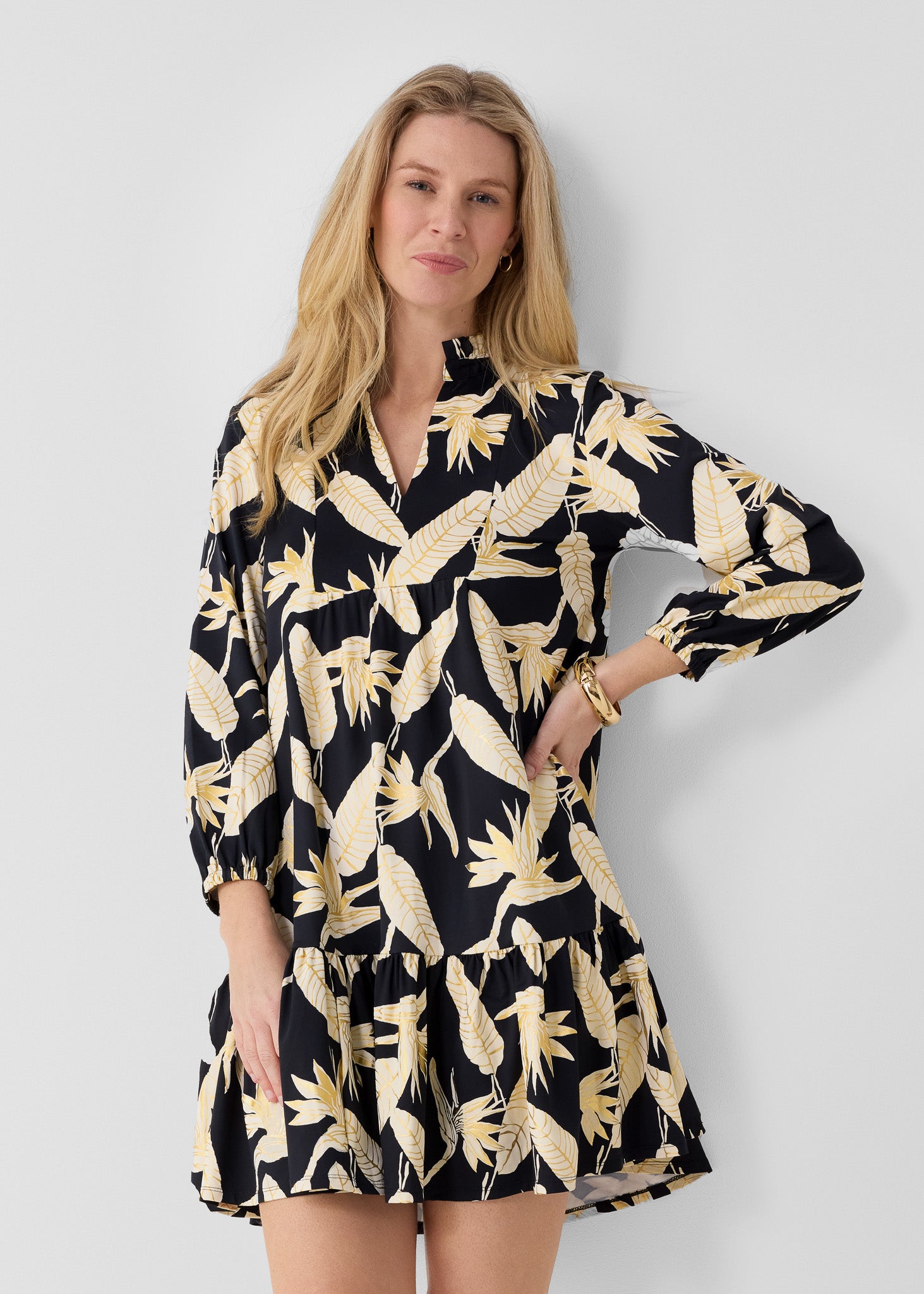 Woman wearing a black dress with gold floral pattern against a white background