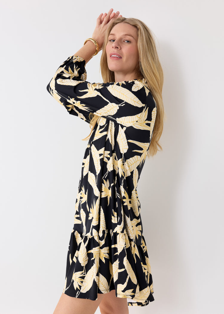 Woman wearing a black dress with gold floral pattern against a white background