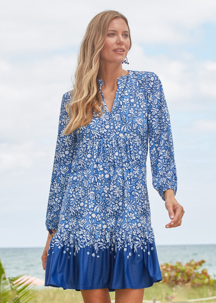 A blonde woman walking at an oceanfront resort wearing Cabana Life's sun protective Seaside Floral Relaxed Dress.