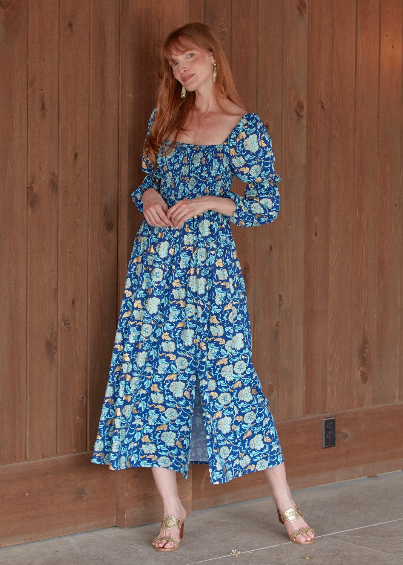 A redhead woman twirling in the sun protective Navy Floral Metallic Puff Sleeve Maxi Dress from Cabana Life in front of wood wall.