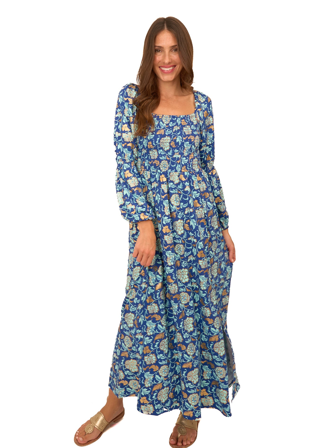 A brunette woman wearing Cabana Life's sun protective Navy Floral Metallic Puff Sleeve Maxi Dress with gold shoes on a white background.