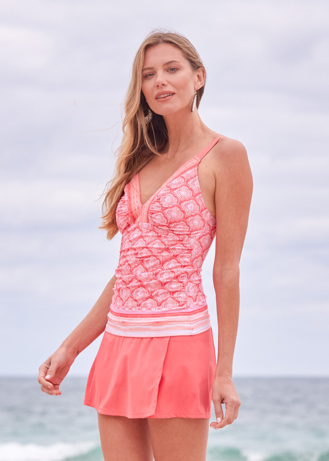 A blonde woman wearing the Cabana Life sun protective Amelia Island Embroidered Tankini Top and Coral Classic Swim Skirt on the beach.