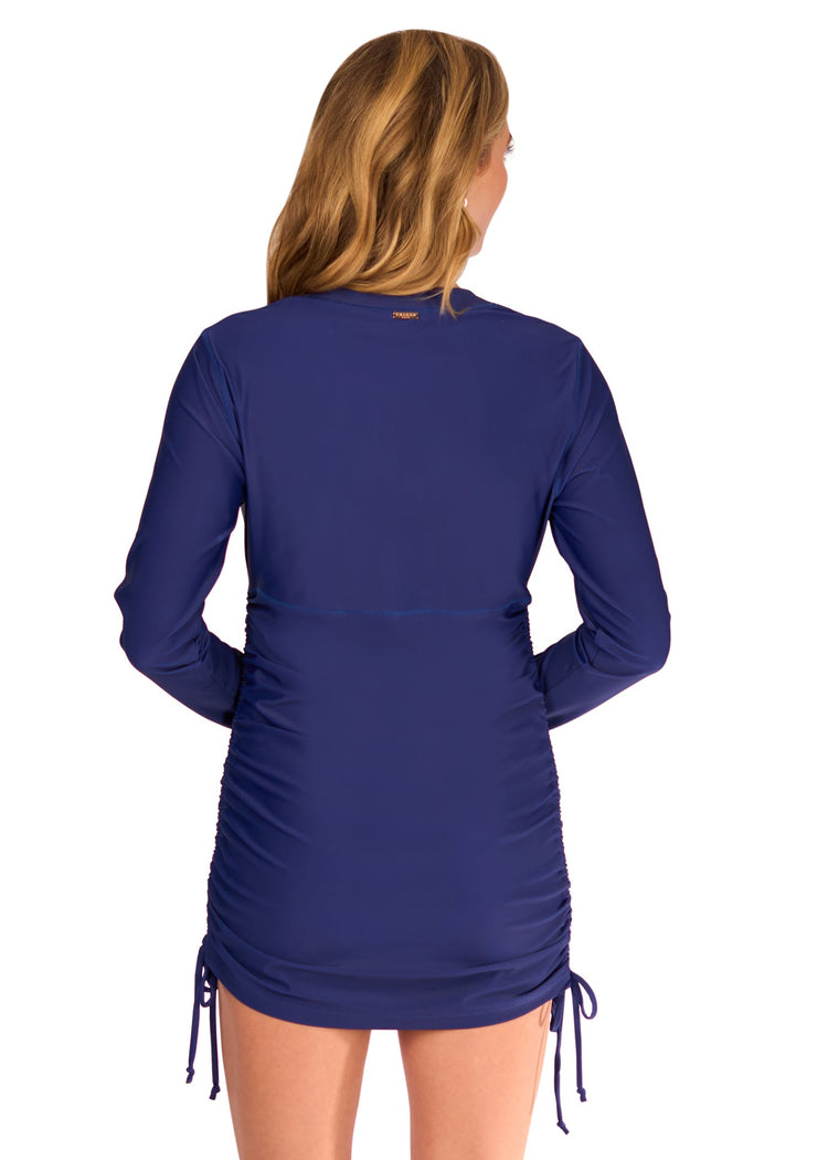 The back of a blonde woman wearing the Cabana Life sun protective Navy Embroidered Convertible Ruched Rashguard as a dress, on a white background.