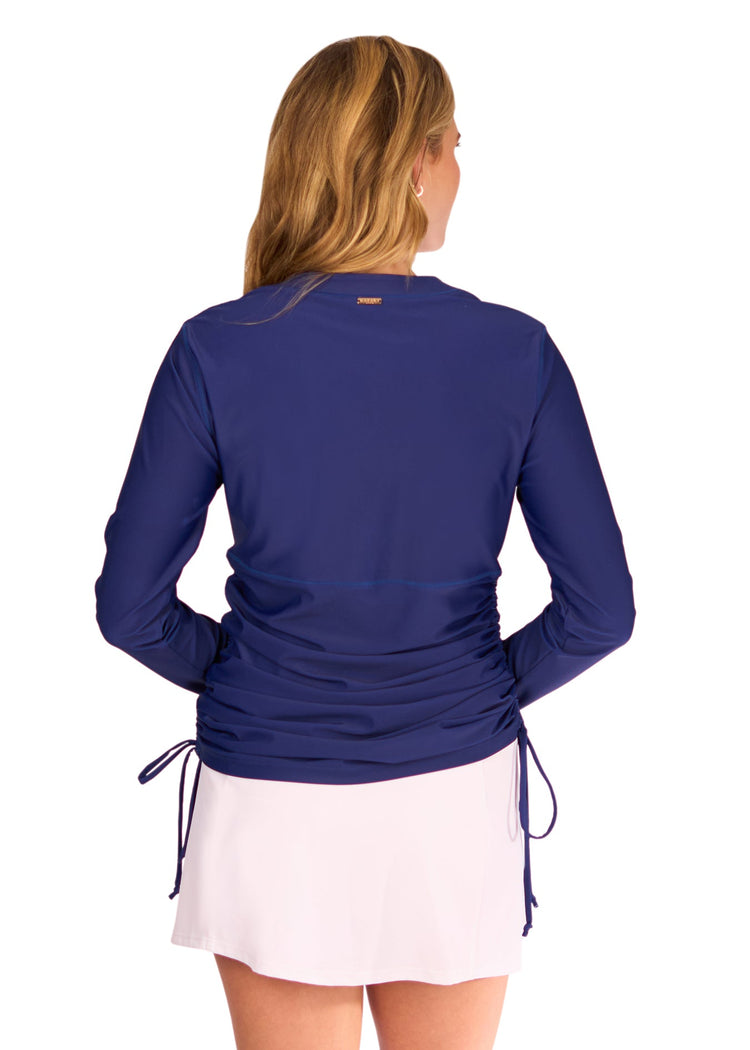 The back of a blonde woman wearing the Cabana Life sun protective Navy Embroidered Convertible Ruched Rashguard with the White Classic Swim Skirt on a white background.