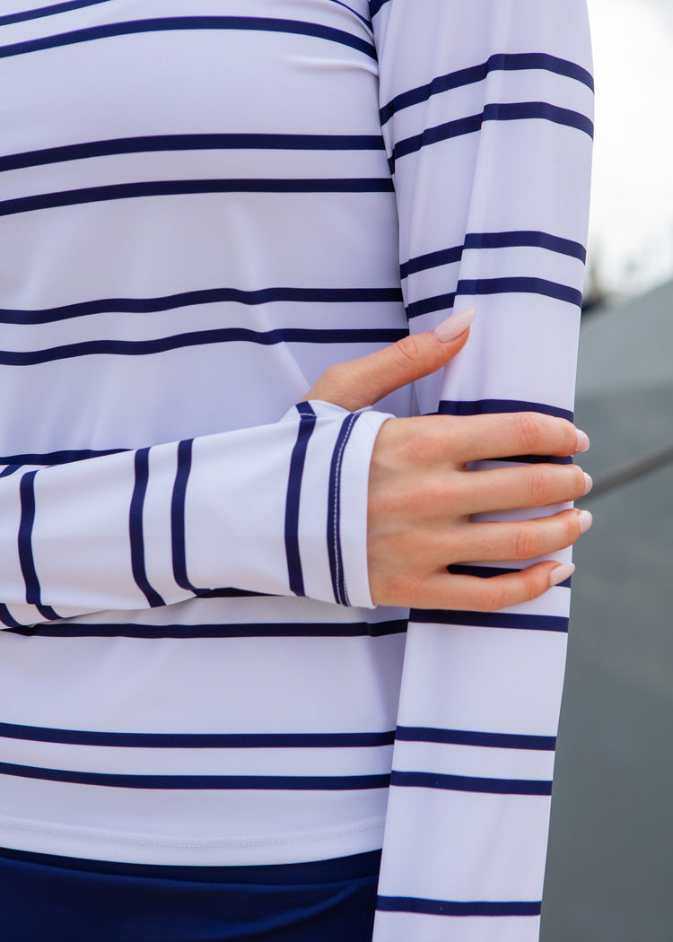 Close-up of a person wearing a white long-sleeve shirt with navy stripes, holding their arm.