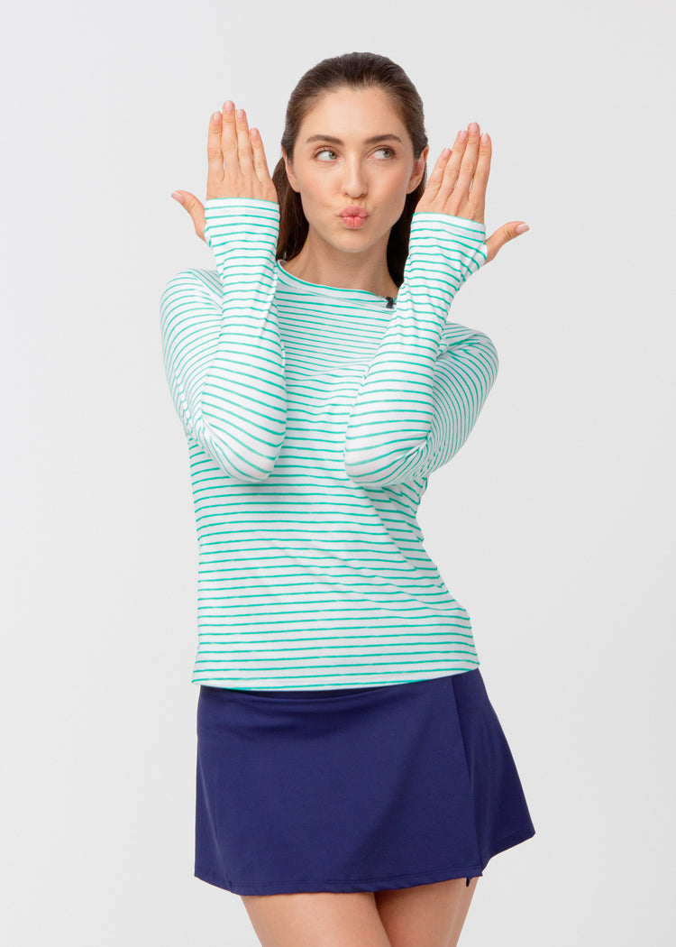 Woman wearing a green and white striped long-sleeve shirt and blue swim skirt on a light gray background