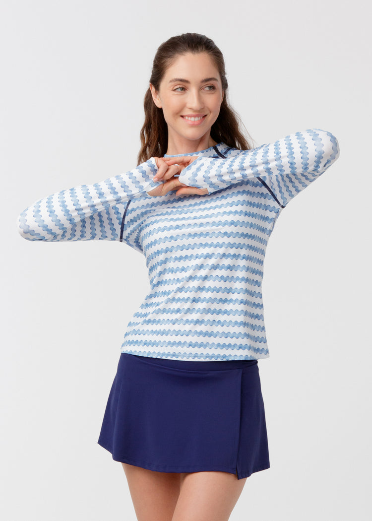Woman wearing a blue and white patterned sweater and navy skirt on a light gray background