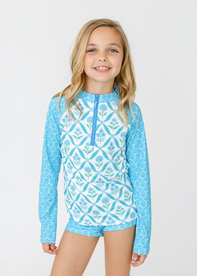 A blonde girl wears Cabana Life's sun safe Girls Rosebay 3-Piece Long Sleeve Rashguard Set.
