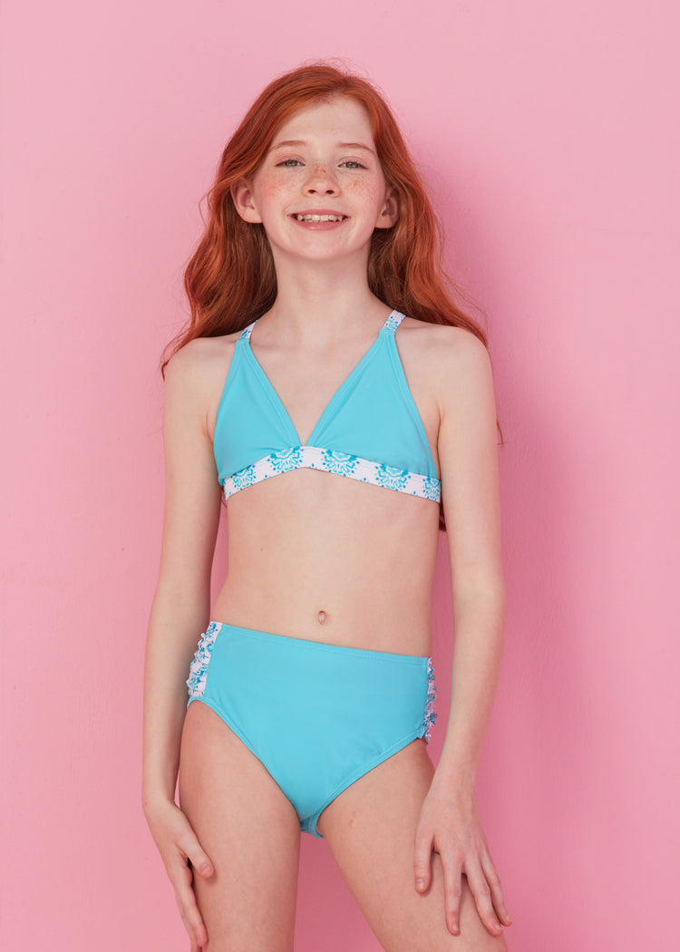 Redhead girl wearing blue bikini set from Girls Amalfi Coast 3-Piece Long Sleeve Rashguard Set in front of pink wall