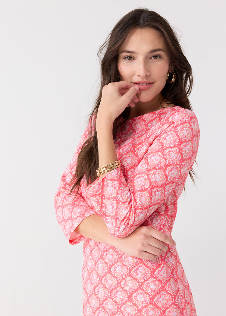 A dark haired woman touching her face wearing the Cabana Life sun protective Amelia Island Cabana Shift Dress with a gold bracelet.