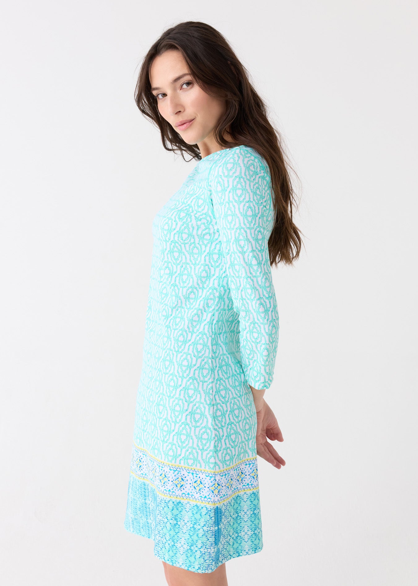 The side of a woman wearing the Cabana Life sun protective Coastal Cottage Cabana Shift Dress with hands behind her back.
