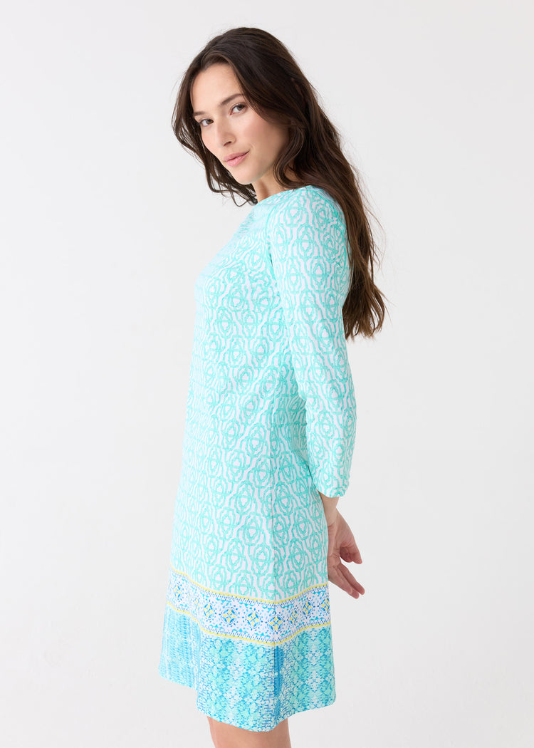 The side of a woman wearing the Cabana Life sun protective Coastal Cottage Cabana Shift Dress with hands behind her back.
