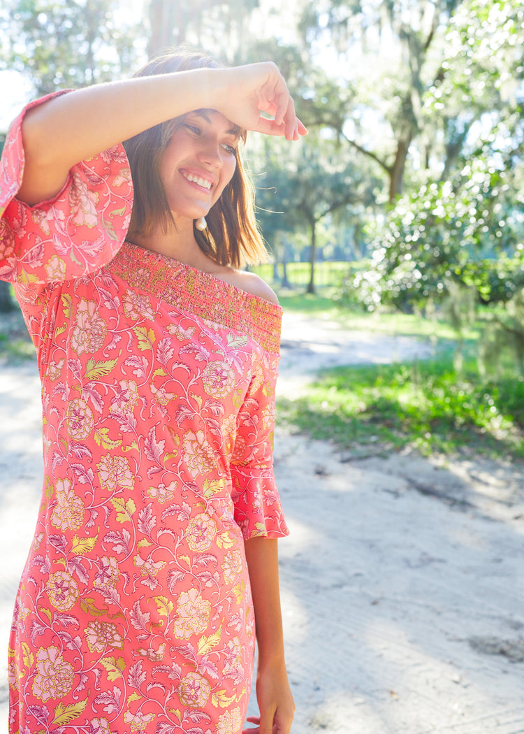 Brunette woman wearing Coral Metallic Off The Shoulder Dress holding hand at head with sun shining.