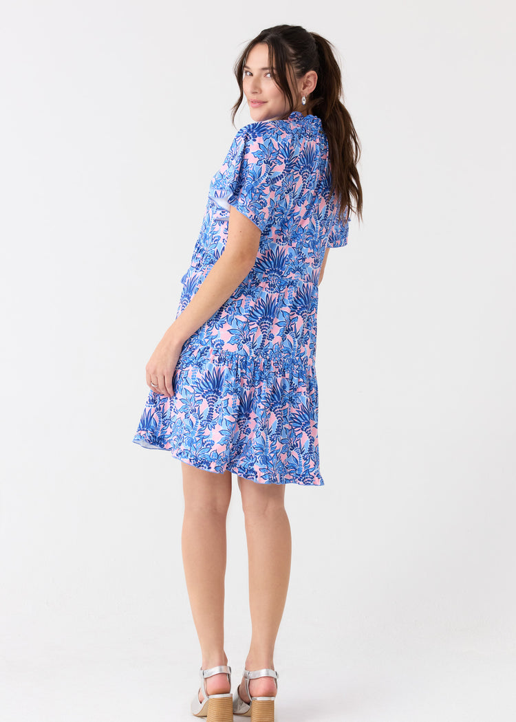 A brunette woman looking back in the Cabana Life sun protective Palm Beach Short Sleeve Tiered Dress, paired with silver sandals.