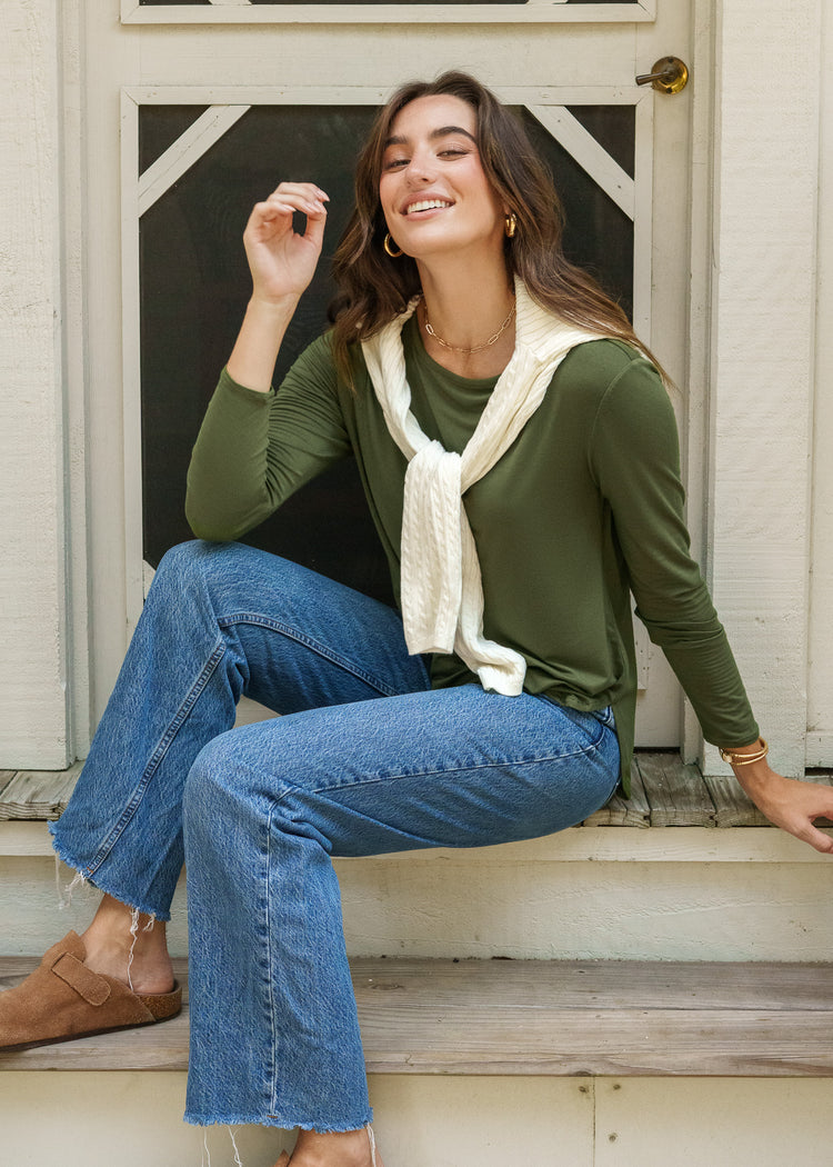 Woman sitting on steps wearing a green top and blue jeans.