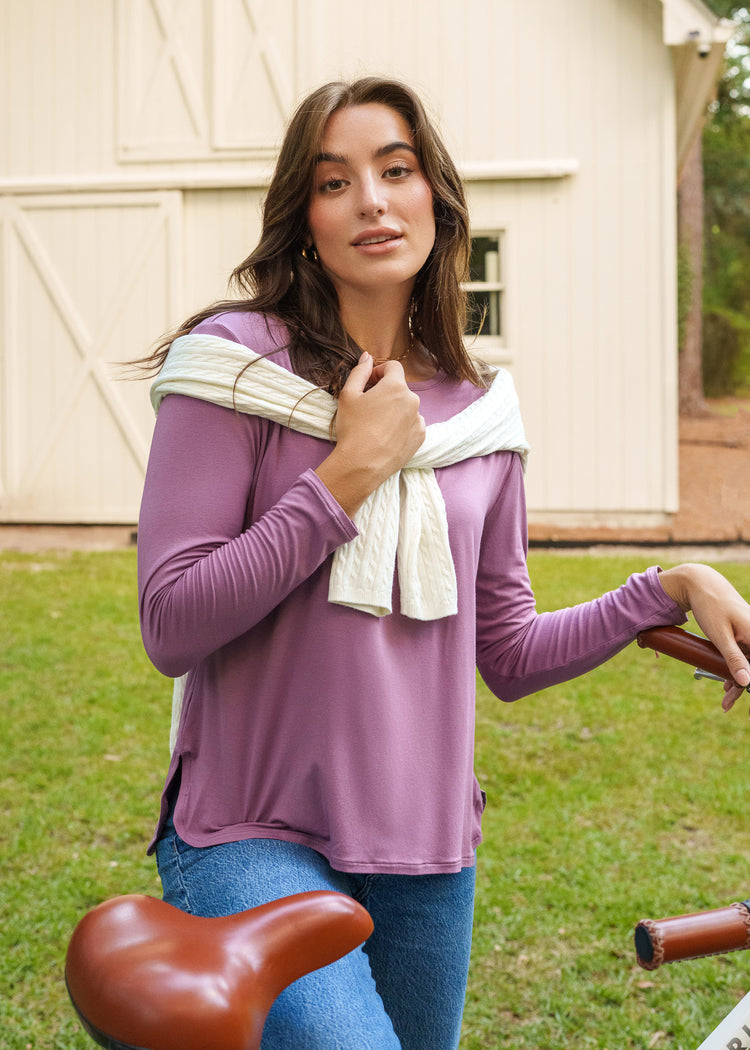 Woman in a purple shirt standing outdoors near a building.