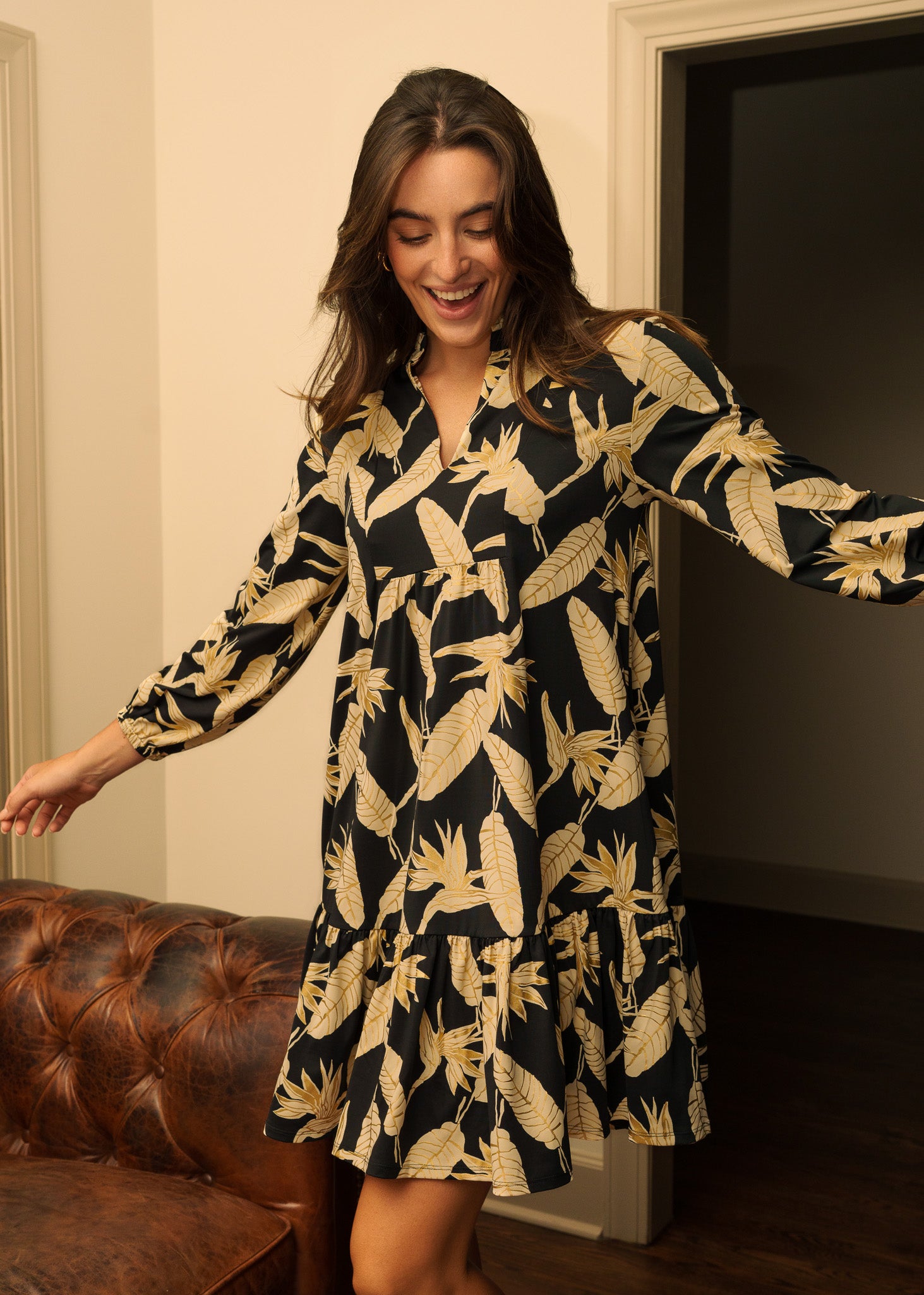 Woman wearing a black dress with gold patterns in a room.
