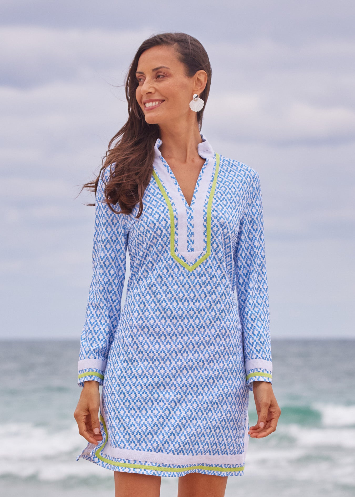 Woman wearing a blue patterned dress with a white shirt underneath, standing on a beach.