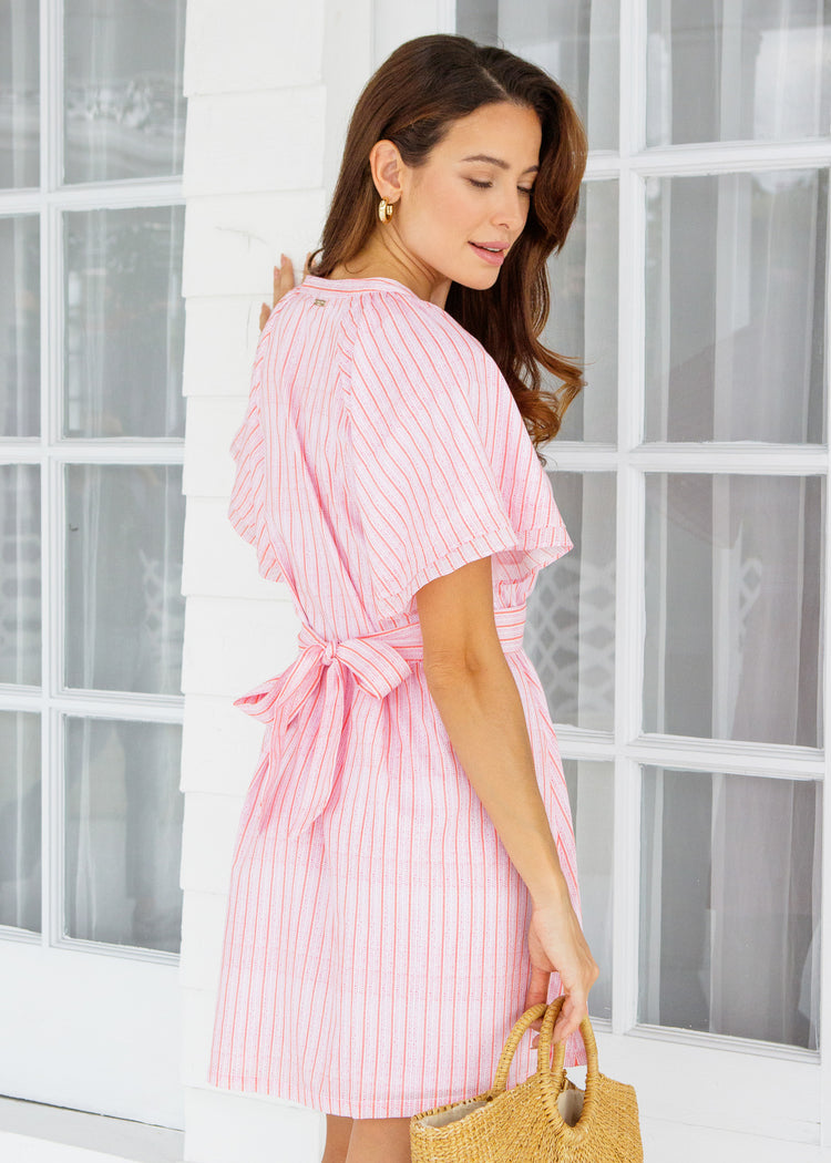 Woman wearing a pink and white striped dress holding a straw bag.