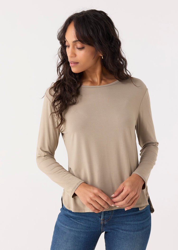A woman wearing a beige long sleeve top with a hi/lo hem, paired with blue jeans.