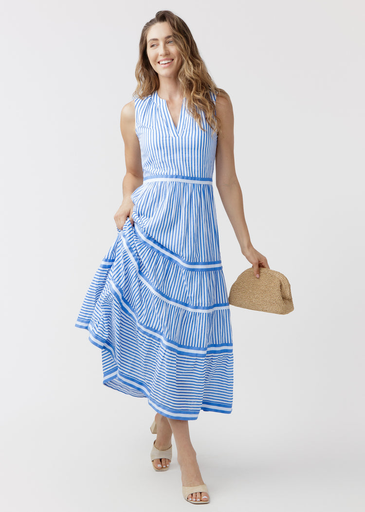 Woman wearing a blue and white striped dress holding a straw bag on a white background