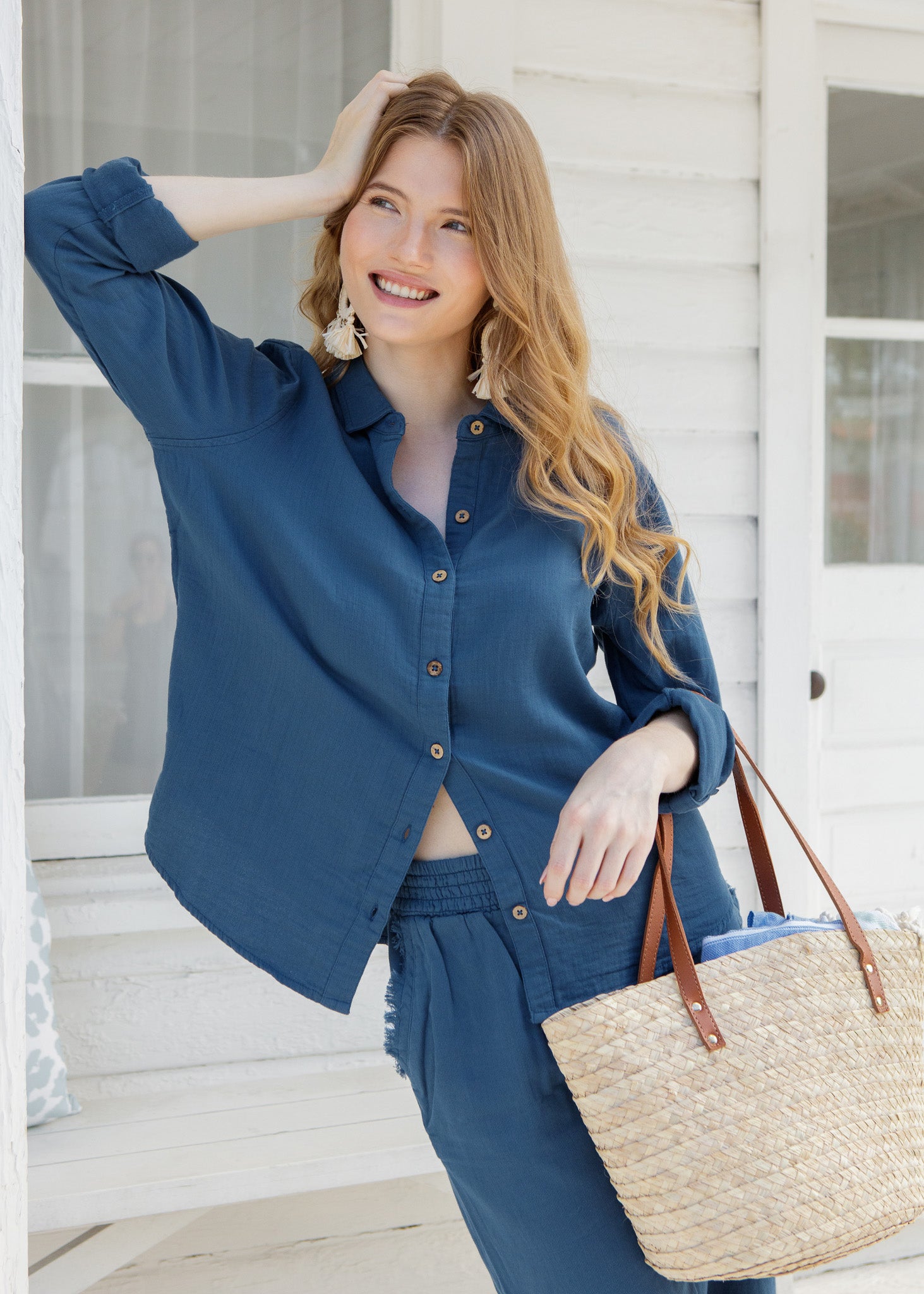 Woman in a blue outfit holding a straw bag on a porch.
