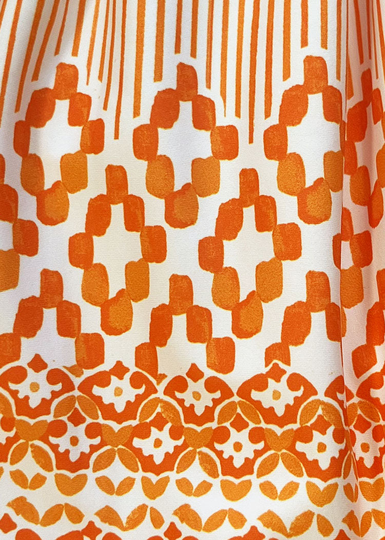 A close-up of a white fabric with a bold orange geometric and floral pattern.