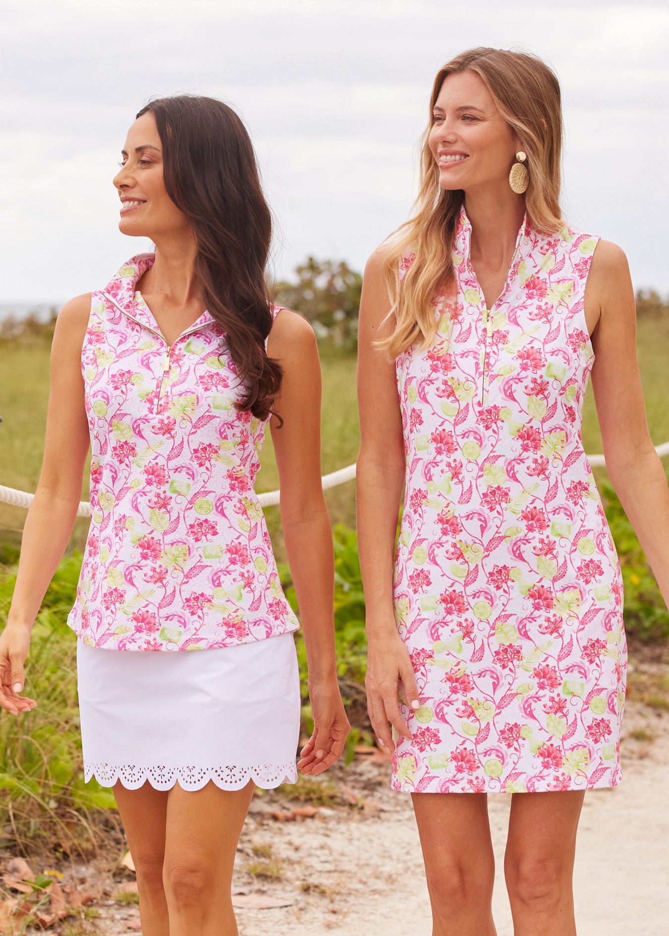 A brunette woman wearing the Cabana Life sun protective Margarita 1/4 Zip Sleeveless Sport Top and White 15" Scallop Skort walking with a women wearing the Margarita 1/4 Zip Sleeveless Sport Dress.