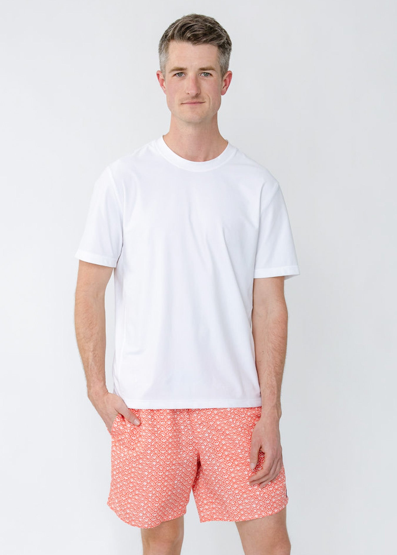 A man wearing the sun protective Men's White Short Sleeve Rashguard with a hand in the pocket of the Men's Amelia Island Swim Trunk from Cabana Life.