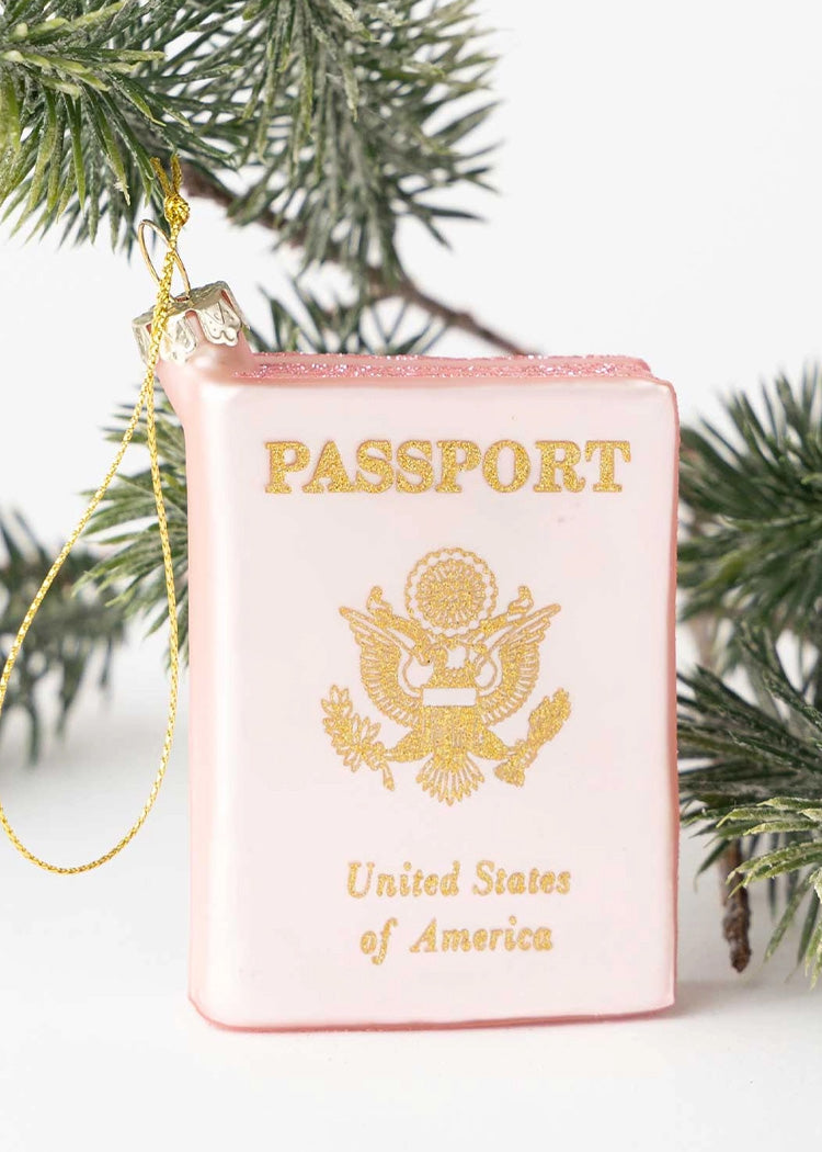 Decorative passport ornament with gold text and a Christmas tree branch in the background