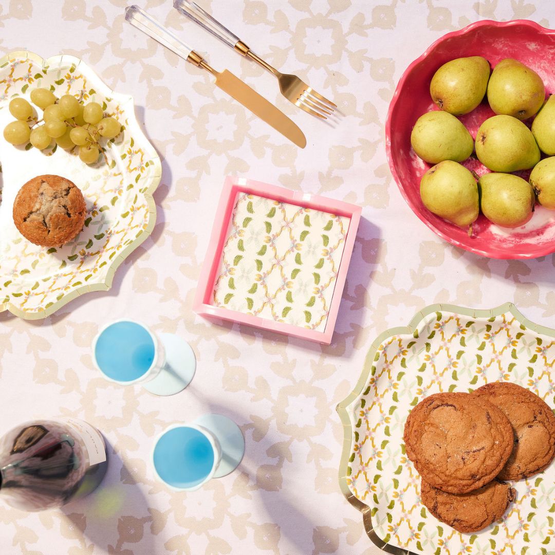 Table setting with cookies, grapes, pears, and glasses on a patterned tablecloth.