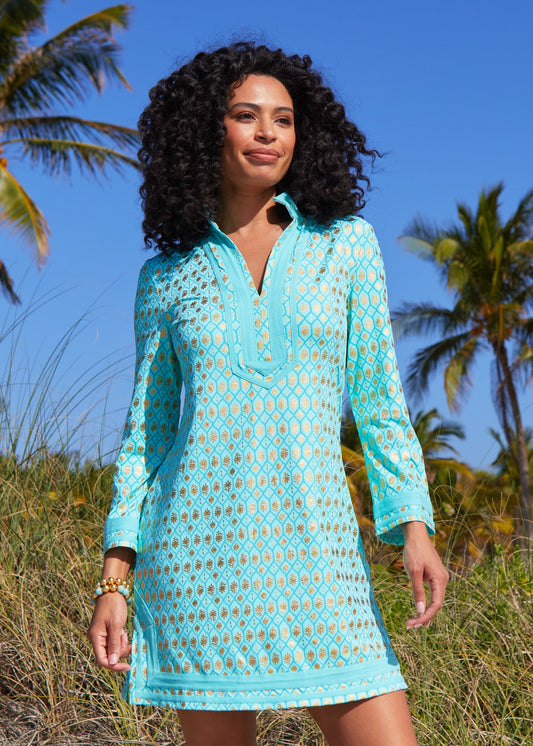 A woman with dark curly hair looking to the side wearing the Aqua Metallic Tunic Dress against sand dunes on the beach.