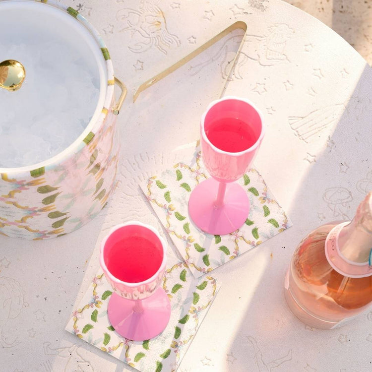 Two pink glasses with a bottle of pink liquid on a textured surface