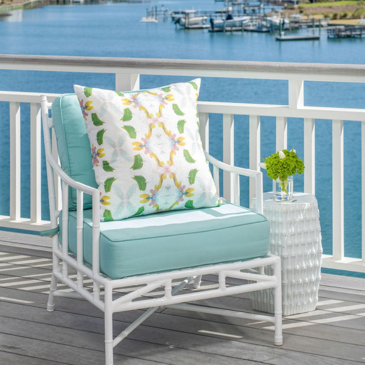 White outdoor chair with blue cushions and a decorative pillow on a deck with a water view.