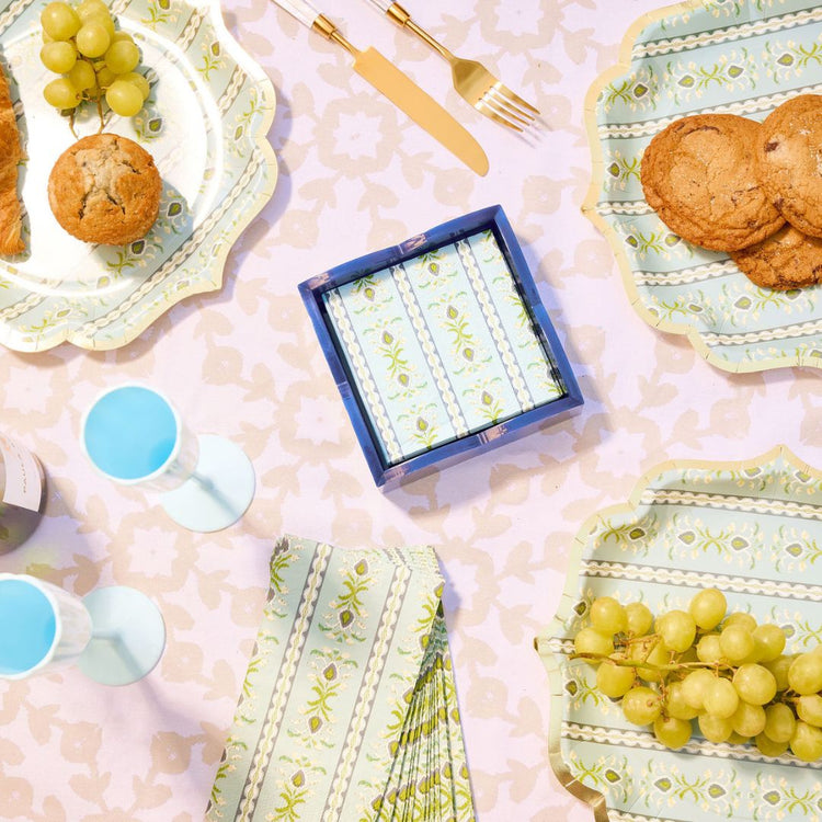 Table setting with plates, grapes, cookies, and a box of tissues on a patterned tablecloth.