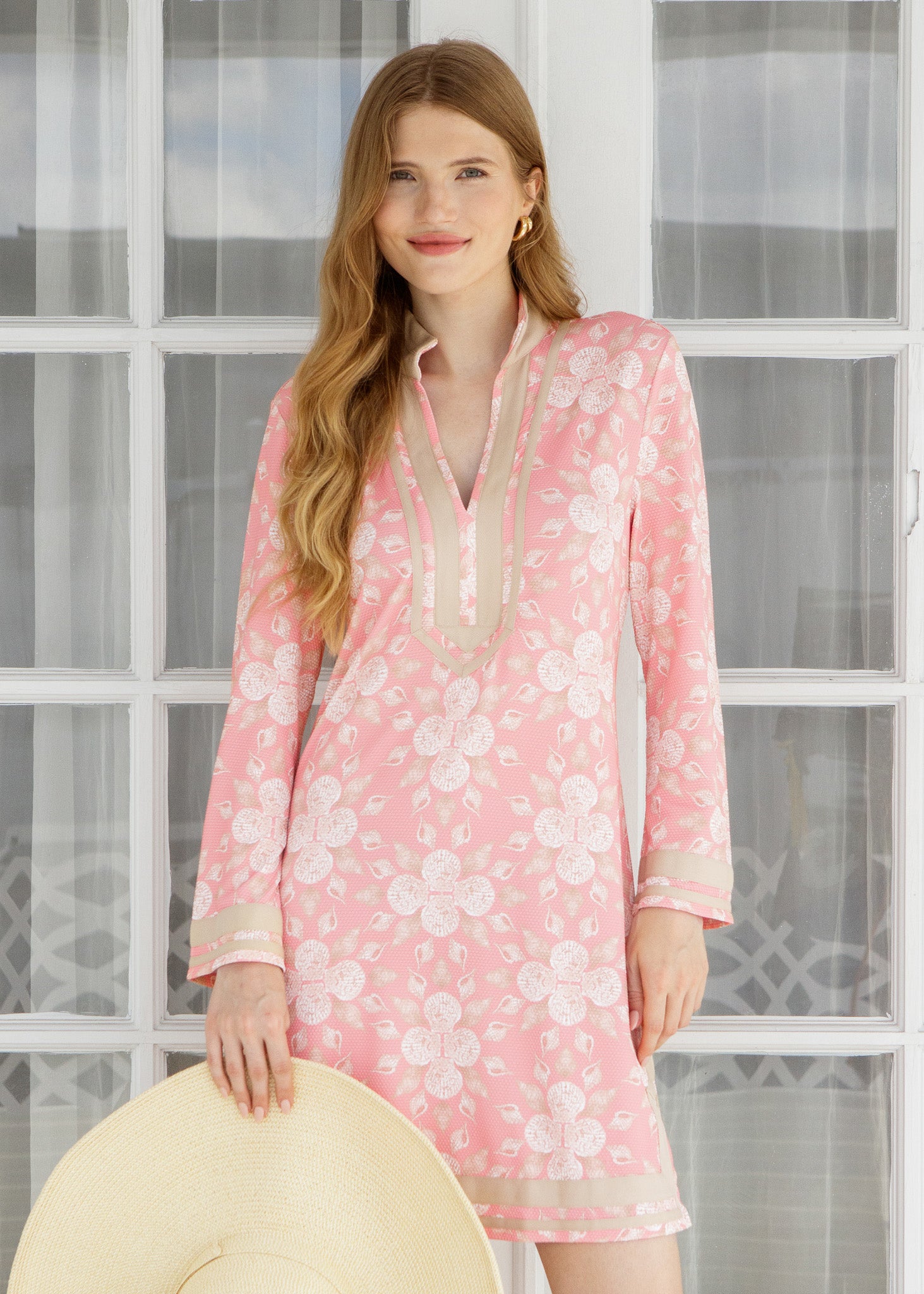 Woman wearing a pink shell dress standing in front of a glass door.