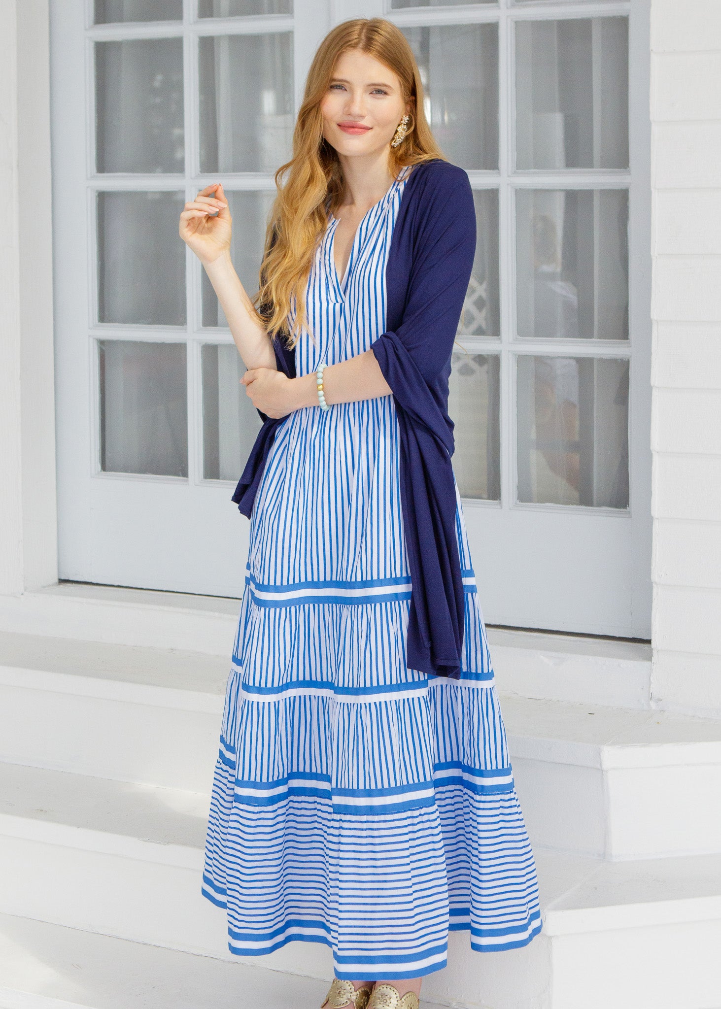 Woman wearing a blue and white striped dress with a navy cardigan in front of a glass door.